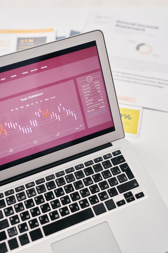 Vue en plongée d’un ordinateur portable affichant des graphiques financiers et des analyses, à côté de documents et de rapports imprimés.